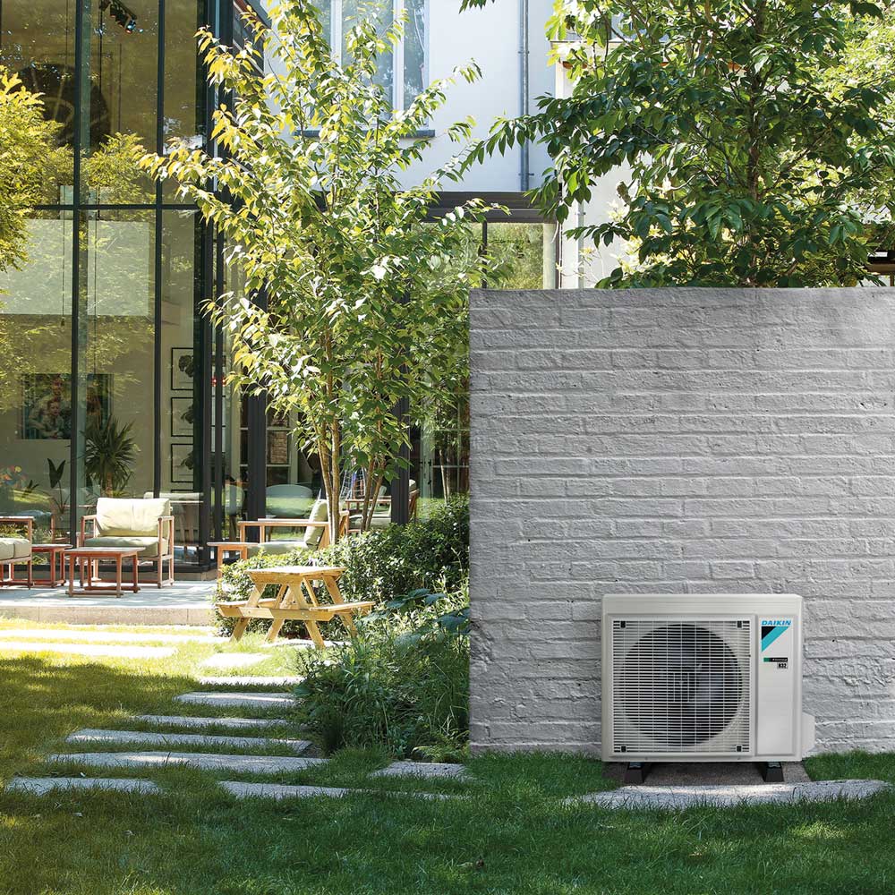 Daikin-Außengerät einer Split-Klimaanlage im Garten vor einer weißen Mauer