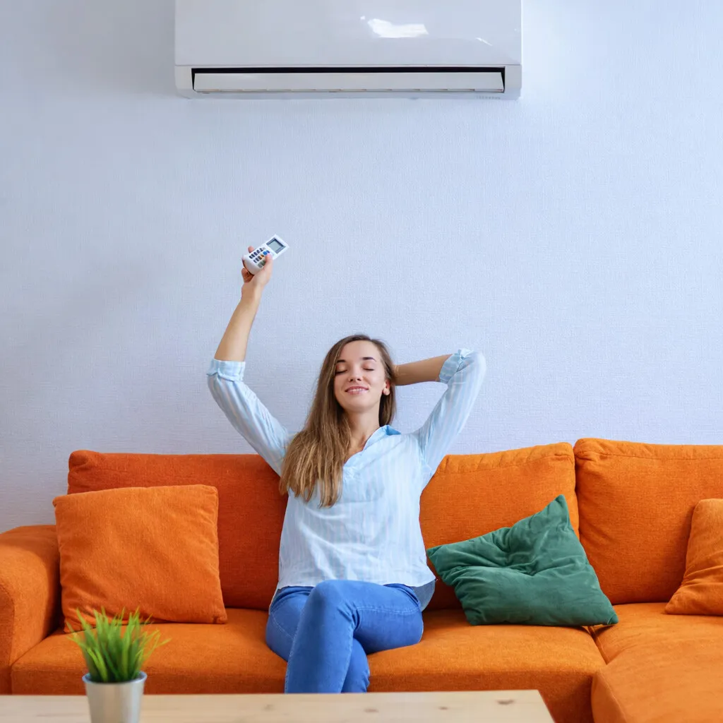 Frau streckt sich entspannt auf dem Sofa, in der Hand die Fernbedienung der Klimaanlage